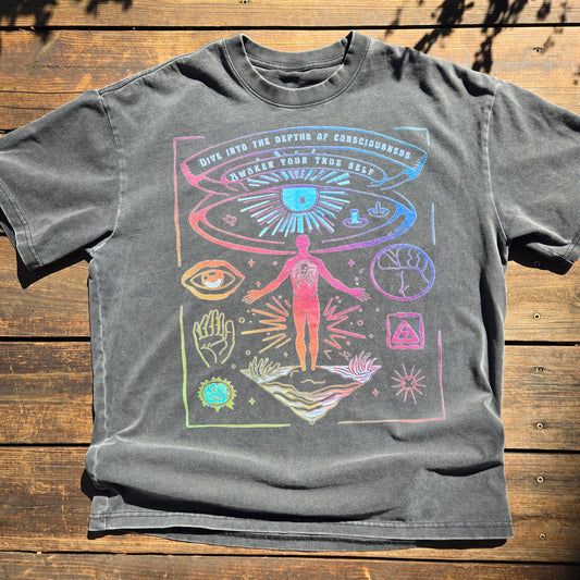 Dark gray Awaken Your True Self vintage wash tee with colorful consciousness-themed print laid flat on wooden deck