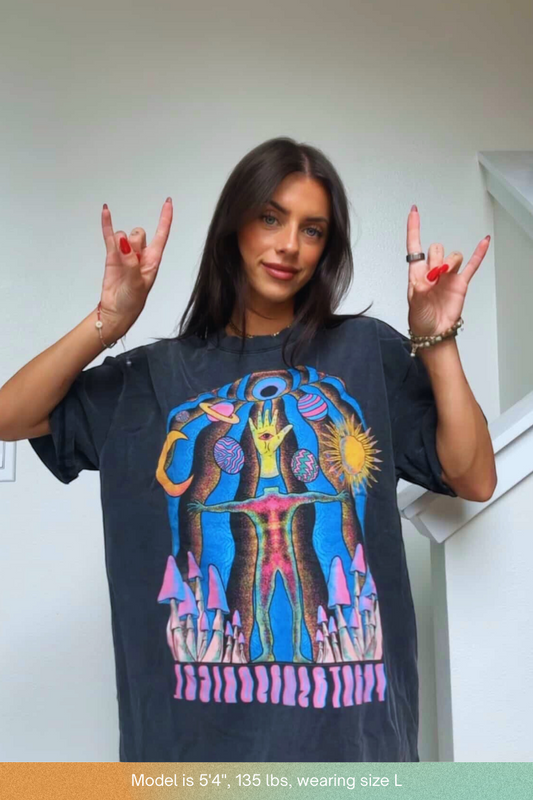 Woman in oversized black Self Actualized tee throwing rock-on hand signs showing psychedelic cosmic graphic