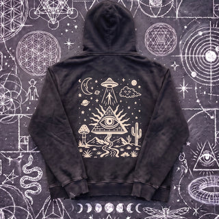 Black Beauty Mystic Signal snow washed heavyweight cotton hoodie laid flat on wet chalk-covered pavement, back view with the cream pyramid, all-seeing eye, UFO and desert print.