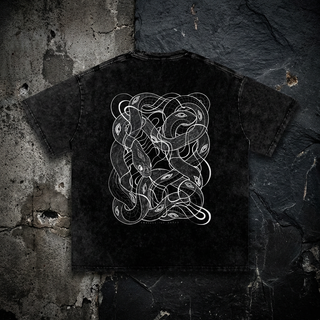 Black snow wash Embrace The Chaos tee, back view on a dark wall, printed with white line art of tangled serpents and eyes, a Patakota collaboration.
