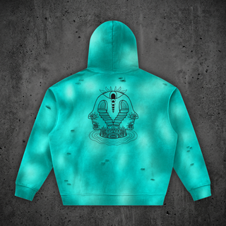 Back of the Enigma hoodie in Phantas Teal with the black line-art Enigma print: an open eye above a spine of moon phases, twin staircases descending between two profile faces toward tall grass rising from rippling water