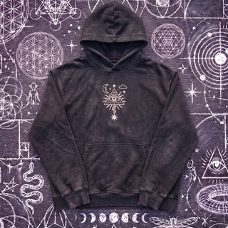 Black Beauty Mystic Signal snow washed heavyweight cotton hoodie laid flat on wet chalk-covered pavement, front view with the cream all-seeing eye in a radiating pyramid printed center chest above the kangaroo pocket.