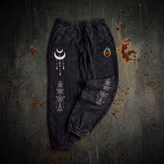 Existential Joggers in black, 420 GSM snow wash, laid flat. Crescent moon with hanging charms on the left thigh, geometry columns down both shins, pH flame on the hip.