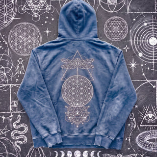 Royal blue Existential snow wash hand-frayed heavyweight hoodie laid flat on wet chalk-covered pavement, showing the cream dragonfly, flower of life and all-seeing-eye celestial print centered on the back.