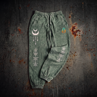 Existential Joggers in blackish green, 420 GSM snow wash, laid flat. Crescent moon with hanging charms on the left thigh, geometry columns down both shins, pH flame on the hip.