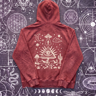 Dark Red Mystic Signal snow washed heavyweight cotton hoodie laid flat on wet chalk-covered pavement, back view with the cream pyramid, all-seeing eye, UFO and desert print.