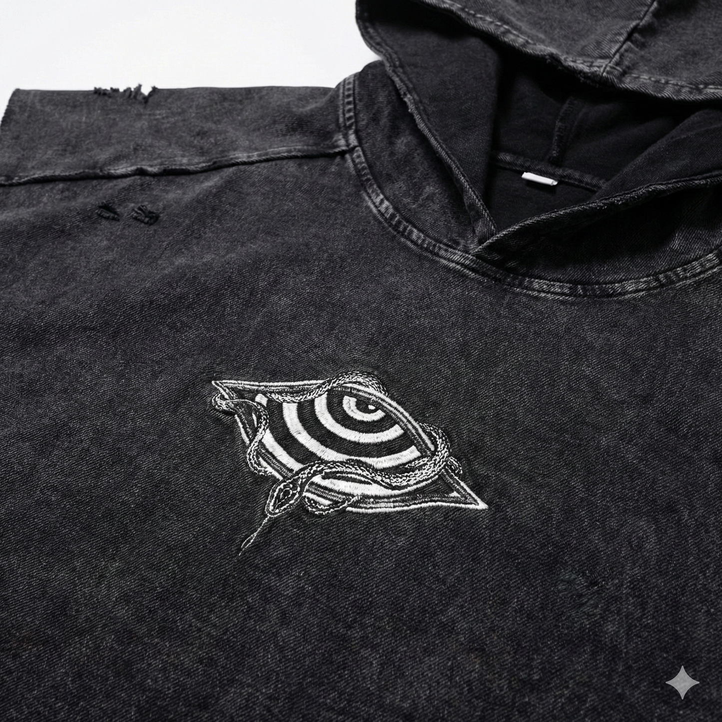 Close-up of embroidered chest logo showing spiraling eye wrapped in snakes on snow wash fabric
