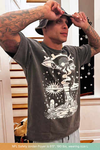Tattooed male model in charcoal wash Paradoxical Perspective tee adjusting cap indoors, size L on 6ft frame