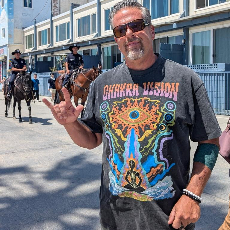 Man flashing shaka sign wearing gray Chakra Vision Fluffy Vintage tee with third eye design on boardwalk