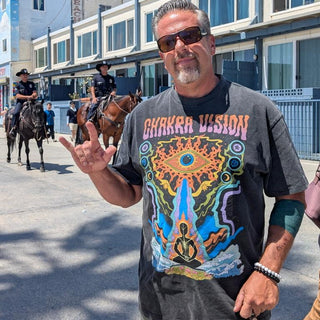 Man flashing shaka sign wearing gray Chakra Vision Fluffy Vintage tee with third eye design on boardwalk
