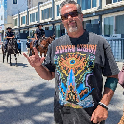 Man flashing shaka sign wearing gray Chakra Vision Fluffy Vintage tee with third eye design on boardwalk