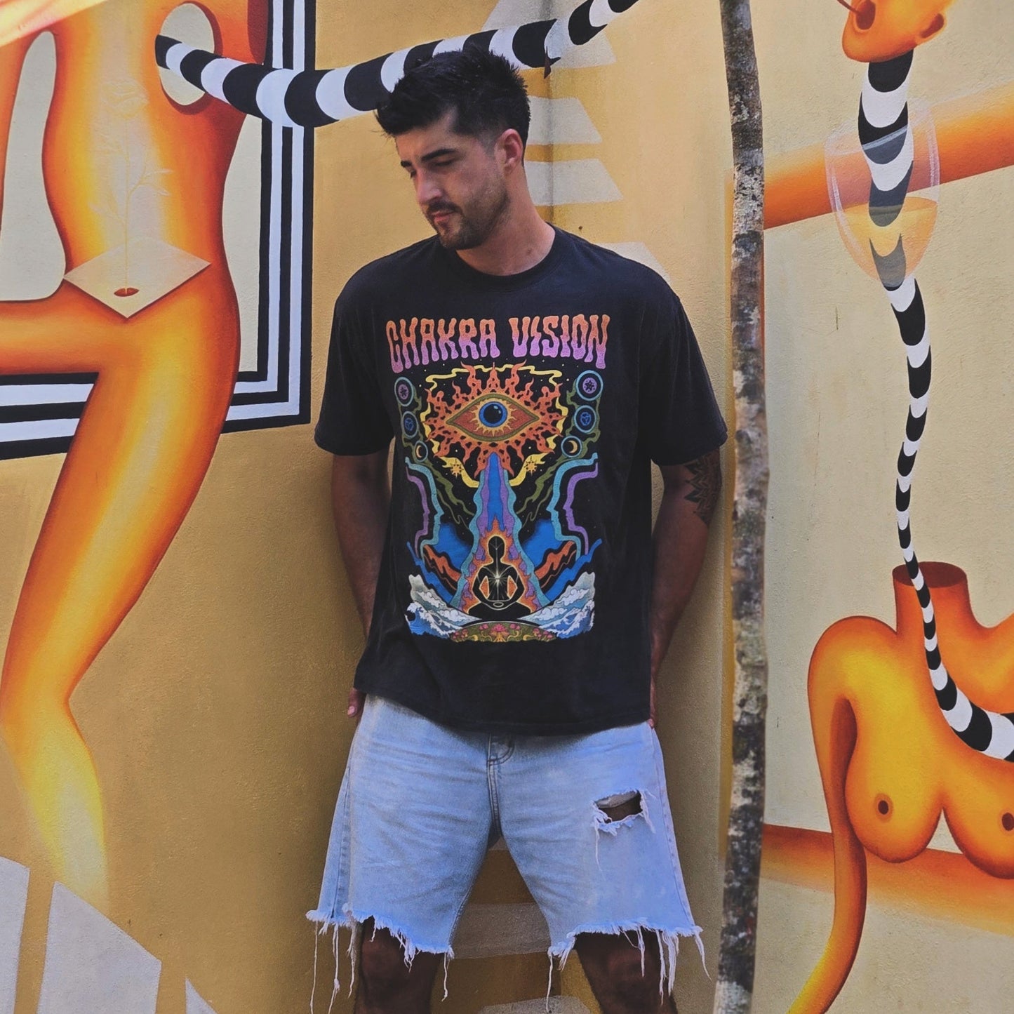 Man wearing black Chakra Vision Fluffy Vintage tee with colorful psychedelic eye and meditation art by mural