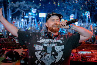 DJ performing at music festival wearing black Lunar Enigma tee with bubbles and crowd behind him