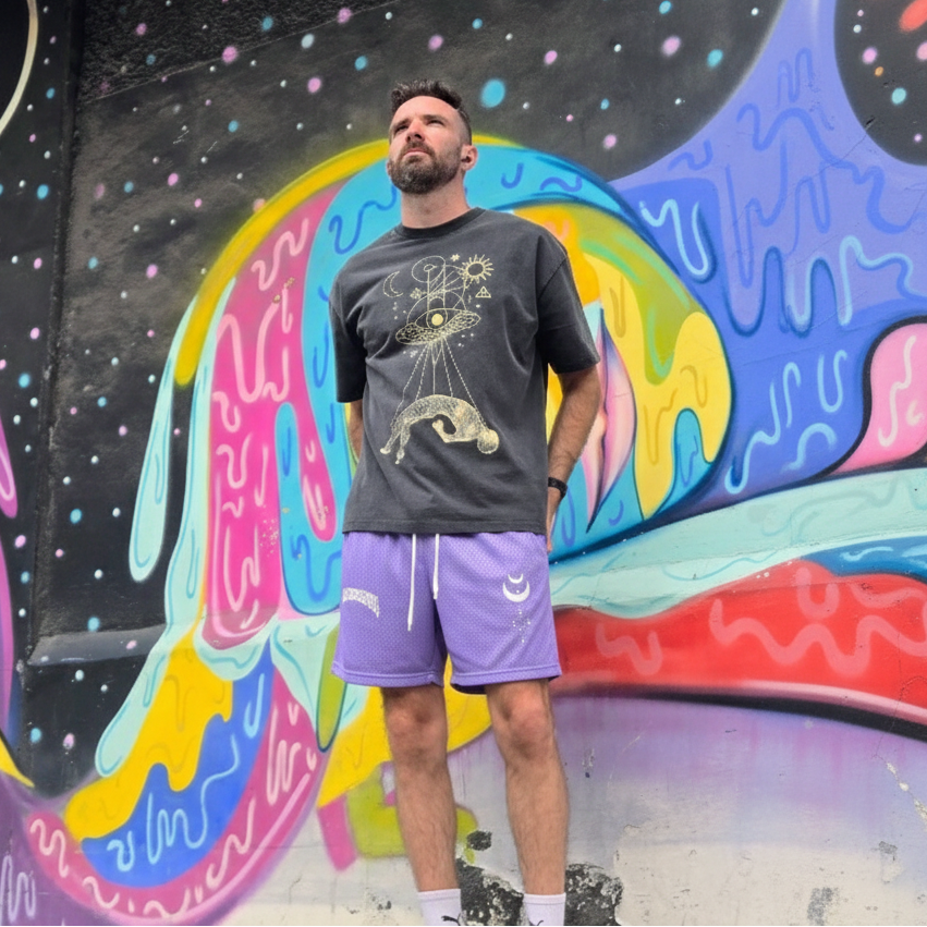 Man wearing Phantasm  purple mesh shorts standing in front of a colorful mural.