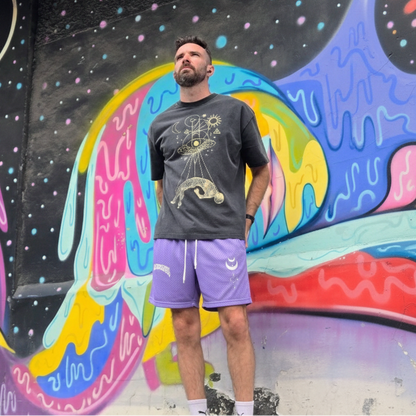 Man wearing Phantasm  purple mesh shorts standing in front of a colorful mural.