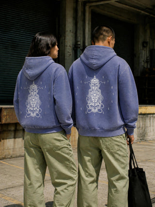 Two models seen from behind wearing the Paradigm mineral wash distressed hoodie in Misty Purple against an industrial loading dock, showing the oversized boxy fit