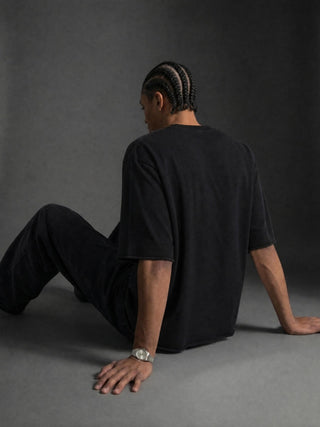 Model wearing the black Dissolution of Ego mineral wash sweater tee, seated, showing the oversized boxy drape