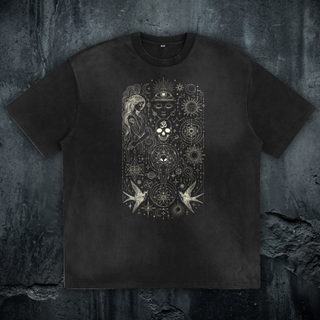 Faded black Ethereal Muse sun fade loose fit heavyweight tee on a concrete wall, printed in cream with a flowing-haired muse, all-seeing eye, om skull and swallows.