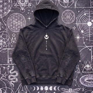 Black Existential snow wash hand-frayed heavyweight hoodie laid flat on wet chalk-covered pavement, front view with the kangaroo pocket and the small cream crescent moon and star stack printed on the chest.