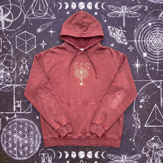Dark Red Mystic Signal snow washed heavyweight cotton hoodie laid flat on wet chalk-covered pavement, front view with the cream all-seeing eye in a radiating pyramid printed center chest above the kangaroo pocket.
