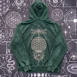 Blackish green Existential snow wash hand-frayed heavyweight hoodie laid flat on wet chalk-covered pavement, showing the cream dragonfly, flower of life and all-seeing-eye celestial print centered on the back.