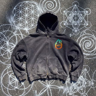 Cosmic Connection ultra heavyweight zip hoodie in washed Black, front view, zipped, on dark asphalt covered in white chalk sacred geometry, with the Phantasmagorical pH logo on the left chest and hand-frayed edges.
