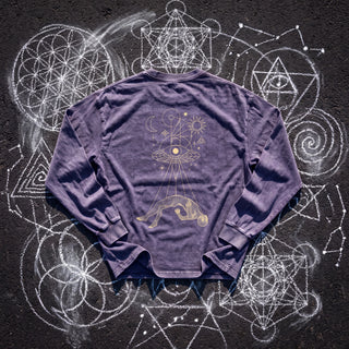 Back of the Dimensional Drift acid wash oversized long sleeve tee in Purple Haze, styled on dark asphalt covered in white chalk sacred geometry, showing a cream and gold eye disc casting light onto a levitating figure.