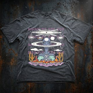 Charcoal Dissolve The Ego fluffy vintage heavyweight tee on rusted metal, printed with a meditating alien ringed like Saturn, repeated Dissolve The Ego text and a pastel desert scene.