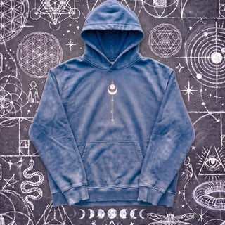 Royal blue Existential snow wash hand-frayed heavyweight hoodie laid flat on wet chalk-covered pavement, front view with the kangaroo pocket and the small cream crescent moon and star stack printed center chest.