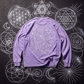 Back of the Embrace The Chaos acid wash oversized long sleeve tee in Purple, styled on dark asphalt covered in white chalk sacred geometry, showing a white line-art panel of intertwined serpents.