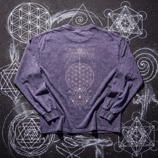 Back of the Existential acid wash oversized long sleeve tee in Purple Haze, styled on dark asphalt covered in white chalk sacred geometry, showing the fine-line dragonfly, triangle and flower of life column print.