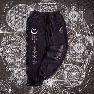 Existential Joggers in black, 420 GSM snow wash, laid flat on chalk sacred geometry. Crescent moon with hanging charms on the thigh, geometry columns down both shins, pH logo on the hip.