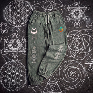 Existential Joggers in blackish green, 420 GSM snow wash, laid flat on chalk sacred geometry. Crescent moon with hanging charms on the thigh, geometry columns down both shins, pH logo on the hip.