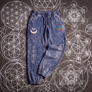 Existential Joggers in royal blue, 420 GSM snow wash, laid flat on chalk sacred geometry. Crescent moon with hanging charms on the thigh, geometry columns down both shins, pH logo on the hip.