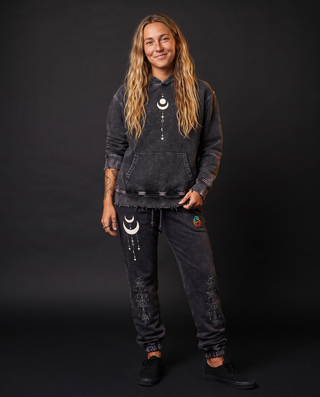 Model 5'9" and 135 lb wearing the charcoal Existential snow wash hand-frayed heavyweight hoodie, hood down, showing the raw frayed hem and the cream crescent moon and celestial stack printed center chest, styled with matching Existential snow wash joggers with cuffed ankles.