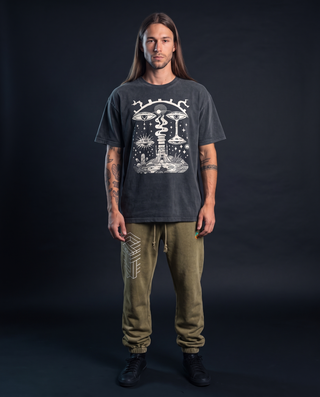 Model 6'0" and 165 lb wearing the charcoal Paradoxical Perspective fluffy vintage heavyweight tee in size L, printed centred on the chest with crying surreal eyes, a tree-stump temple, sun-eye and mushrooms, styled with olive Paradigm snow wash joggers with cuffed ankles.