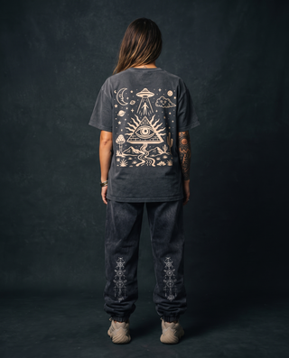 Back view of a model 5'4" and 125 lb wearing the charcoal Mystic Signal fluffy vintage wash heavyweight tee in size S, printed across the back in cream with a UFO beaming up a figure, an all-seeing eye pyramid and a starlit desert scene, styled with charcoal Existential snow wash joggers.