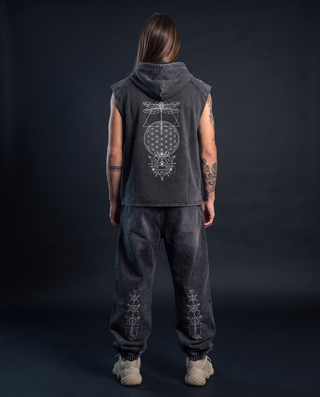 Back view of a model 6'0" and 165 lb wearing the charcoal Existential snow washed boxy hooded tank top in size L, hood down, printed across the back in white with a dragonfly, Flower of Life circle and all-seeing eye mandala, styled with matching Existential snow wash joggers.
