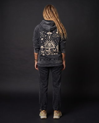 Back view of a model 5'9" and 135 lb wearing the full Mystic Signal Snow Wash Set — black snow washed heavyweight hoodie in size L, hood down, printed across the back in cream with a UFO beaming up a figure, an all-seeing eye pyramid and a starlit desert of cacti and mushrooms, layered over the matching snow wash tee showing below the hem.