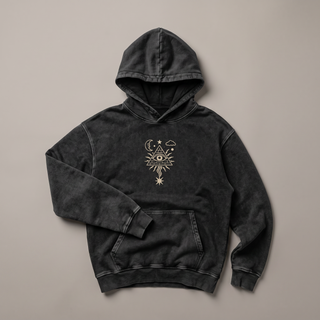 Black snow washed Mystic Signal heavyweight hoodie crumpled into a styled flat lay on a warm grey studio sweep, one sleeve folded across the body and the hood standing soft, with the small cream all-seeing eye in a radiating triangle printed on the chest.