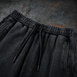 Close-up of the drawstring elastic waistband and slanted side pocket on the black snow wash Existential heavyweight joggers, shot on dark weathered steel.