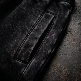 Close-up of the side seam and pocket topstitching on the black snow wash Existential heavyweight joggers, shot on dark weathered concrete.