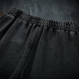 Close-up of the gathered rear elastic waistband on the black snow wash Existential heavyweight joggers, shot on dark weathered concrete.