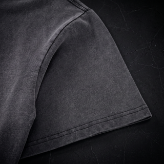 Close-up of the dropped shoulder seam and short sleeve hem on a Phantasmagorical fluffy vintage washed heavyweight tee, shot on dark charcoal stone.