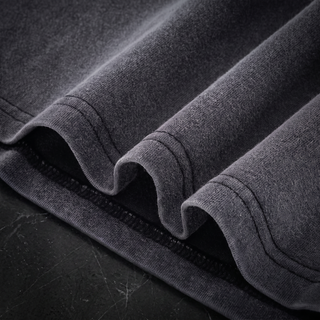 Close-up of the layered bottom hem and double-needle stitching on a Phantasmagorical fluffy vintage washed tee, shot on dark charcoal stone.