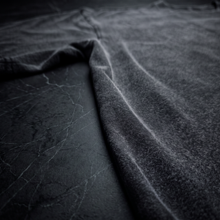 Low three-quarter view along the sleeve of a Phantasmagorical fluffy vintage washed tee on dark charcoal stone, showing the brushed pile and shoulder seam.