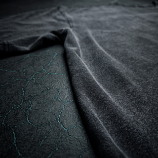Low three-quarter view along the sleeve of the Existential fluffy vintage washed tee on dark charcoal stone, showing the brushed pile and shoulder seam.