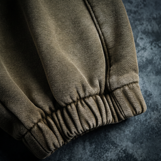 Close-up of the ribbed elasticated ankle cuff on the Paradigm heavyweight joggers, shot on a weathered bluestone wall.