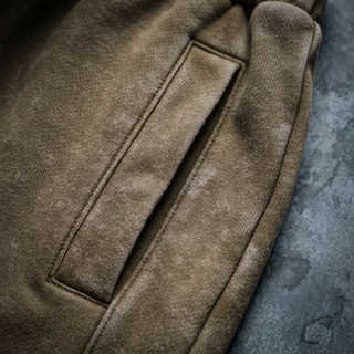 Close-up of the side seam and pocket topstitching on the Paradigm heavyweight joggers, shot on a weathered bluestone wall.