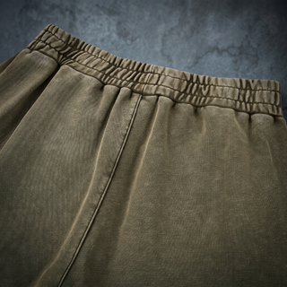Close-up of the gathered rear elastic waistband on the Paradigm heavyweight joggers, shot on a weathered bluestone wall.